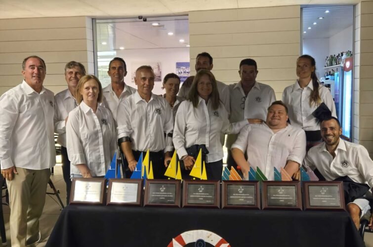 Un grupo de diez personas con ropa blanca posando tras una mesa con varios premios y banderas pequeñas de diferentes colores.