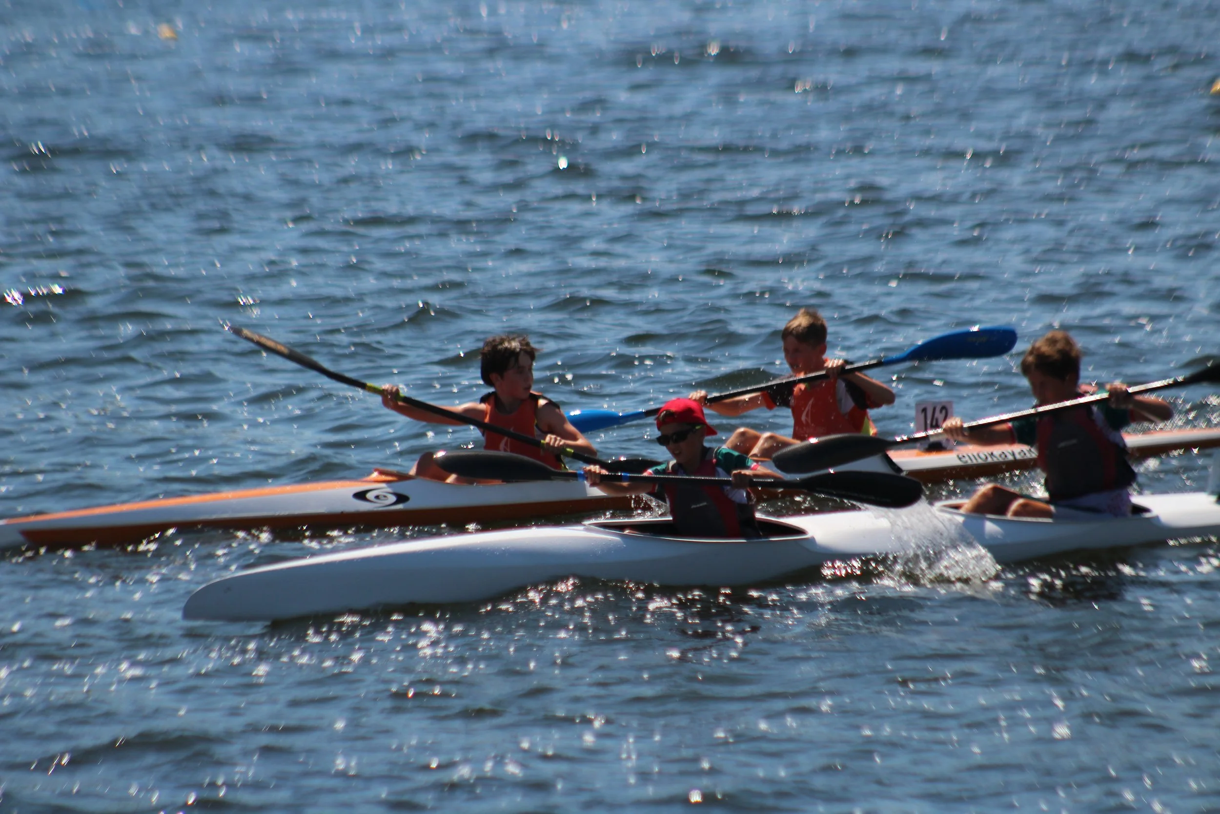 Niños compitiendo en una carrera de kayak en un cuerpo de agua.