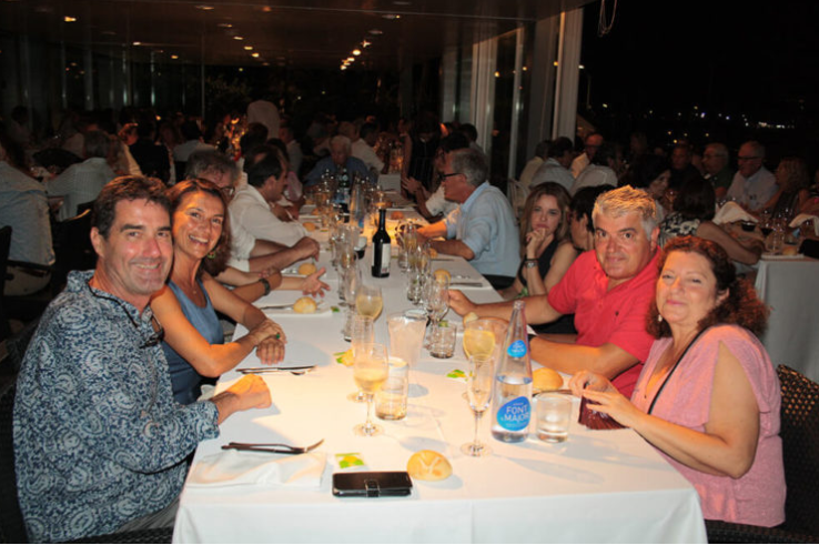 Grupo de personas sentadas en una mesa durante una cena en un restaurante elegante, en un ambiente bien iluminado y con vista a un exterior oscuro.