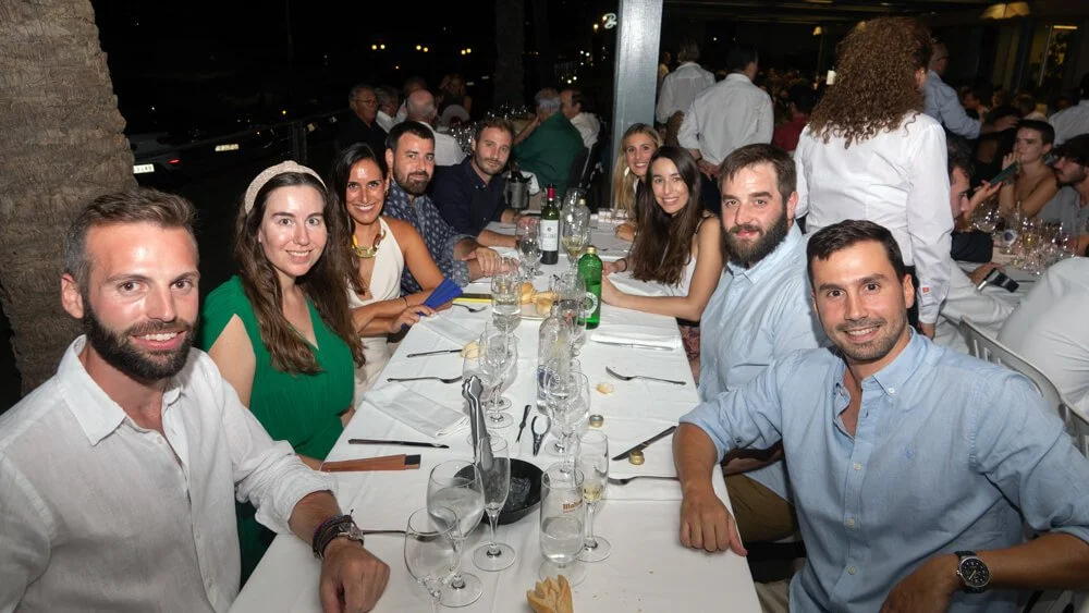 Grupo de personas sentadas en una mesa de restaurante durante la noche, celebrando y sonriendo.