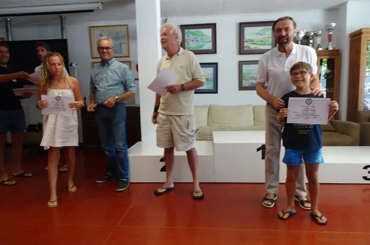 Niños y adultos en una ceremonia de premiación, con niños sosteniendo certificados, en un entorno con decoración de cuadros y trofeos.