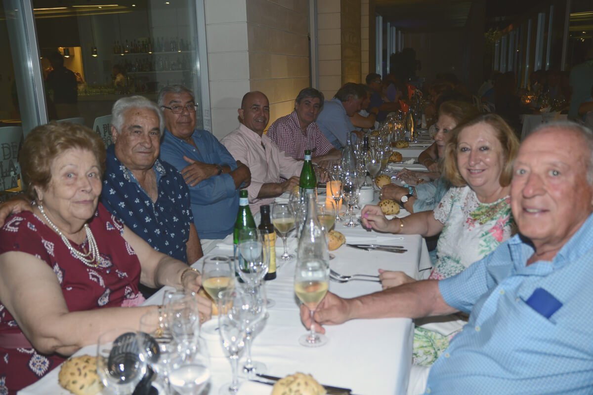 Un grupo de personas sentadas en una mesa larga en un restaurante, disfrutando de una comida y bebida en un ambiente elegante.