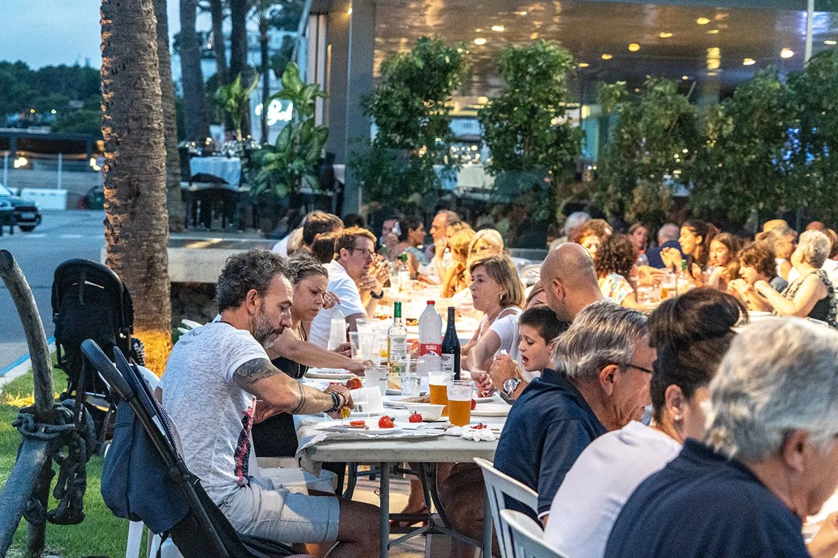 Gente cenando al aire libre en una terraza por la tarde, con muchas mesas llenas.