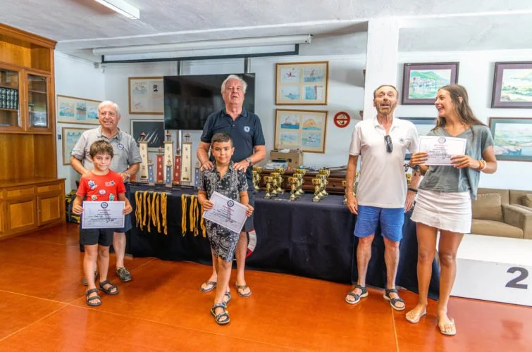 Grupo de personas en una ceremonia de premiación, con niños y adultos, en una sala con decoraciones y diplomas.