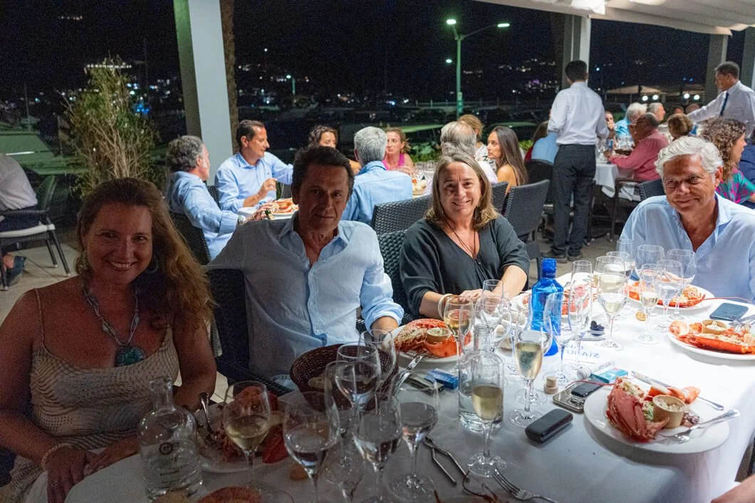 Grupo de personas en una cena en un restaurante con vista nocturna, comiendo mariscos y bebiendo vino.