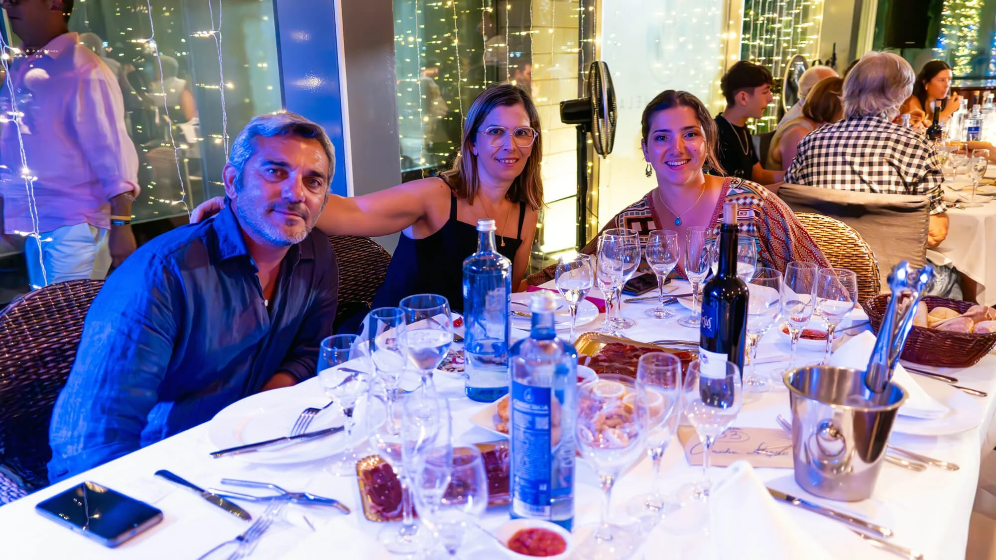 Personas cenando en un restaurante elegante con decoraciones navideñas, platos de comida, vinos y agua en una mesa.