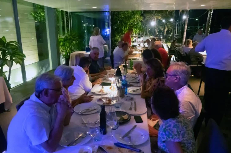 Personas sentadas en una mesa en un restaurante, compartiendo una comida, con decoración y vegetación alrededor.