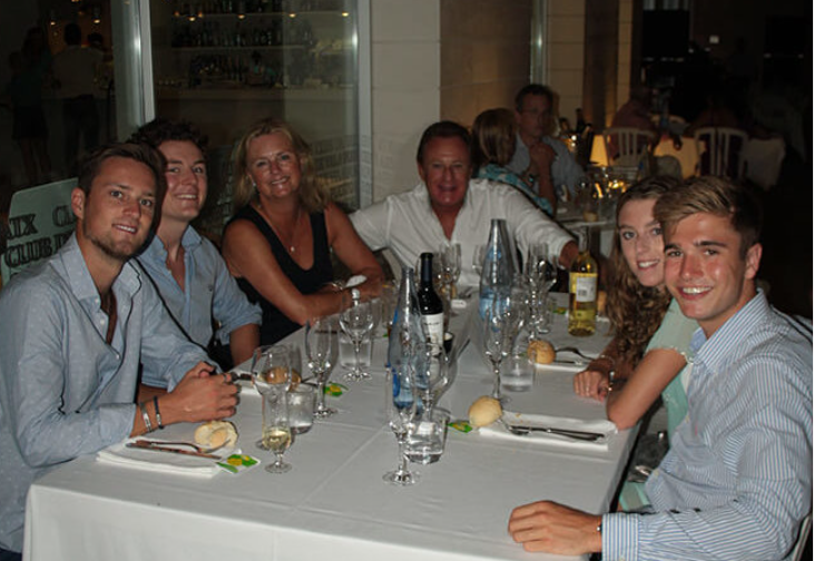 Grupo de seis personas sentadas en una mesa de restaurante en la noche, con bebidas y comida, sonriendo y disfrutando de una cena juntos.