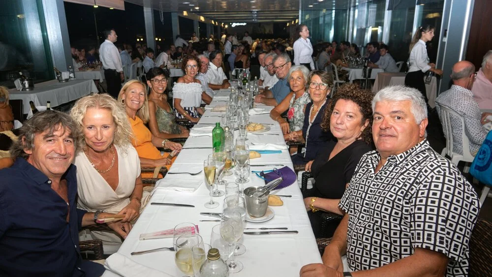Grupo de personas sentadas en una mesa larga en un restaurante durante una celebración, con varias copas y botellas sobre la mesa.