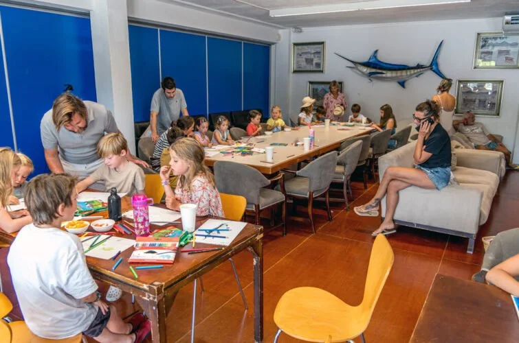 Niños en una clase de arte en un aula con adultos supervisando, decoraciones marinas en la pared.