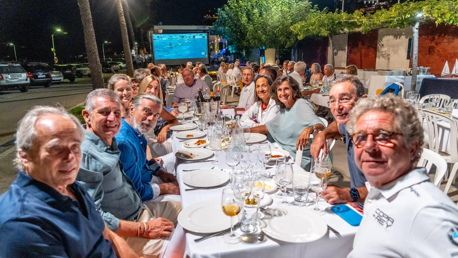 Grupo de personas disfrutando una cena al aire libre con manyas luces y proyección en la pared