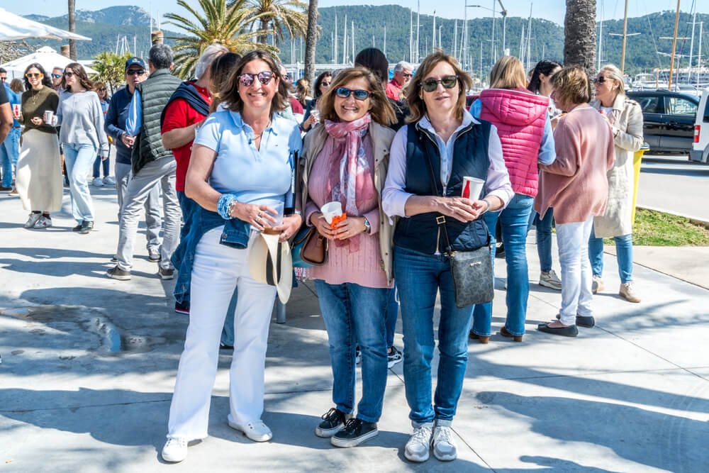 Grupo de personas sonriendo y posando en un muelle al aire libre con árboles y barcos al fondo.
