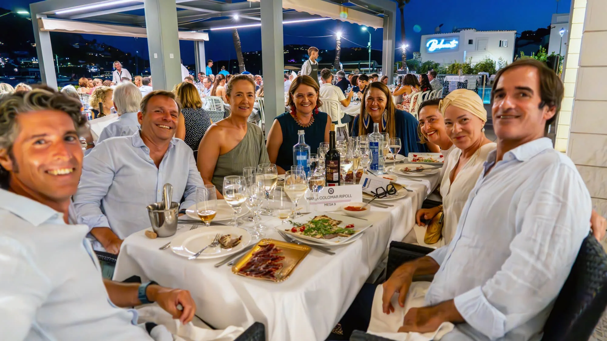 Grupo de personas sentadas en una mesa en un restaurante al aire libre en la noche, disfrutando de comida y bebida