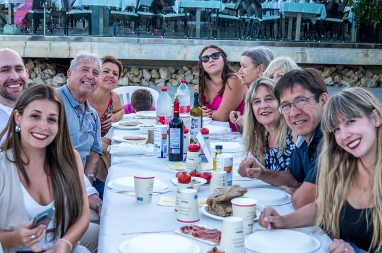 Familia o grupo de amigos sentados en una mesa al aire libre, disfrutando de una comida juntos.