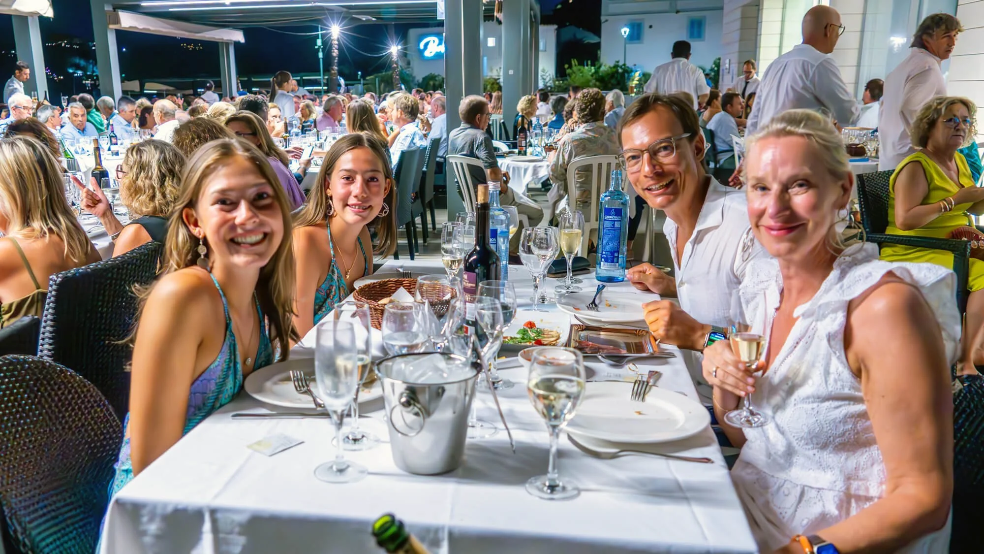 Personas disfrutando una cena en un restaurante al aire libre, con muchas mesas llenas y ambiente animado por la noche.