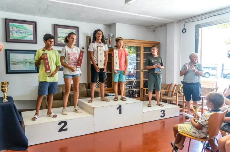 Niños en el podio recibiendo premios en una ceremonia de premiación, con adultos observando.