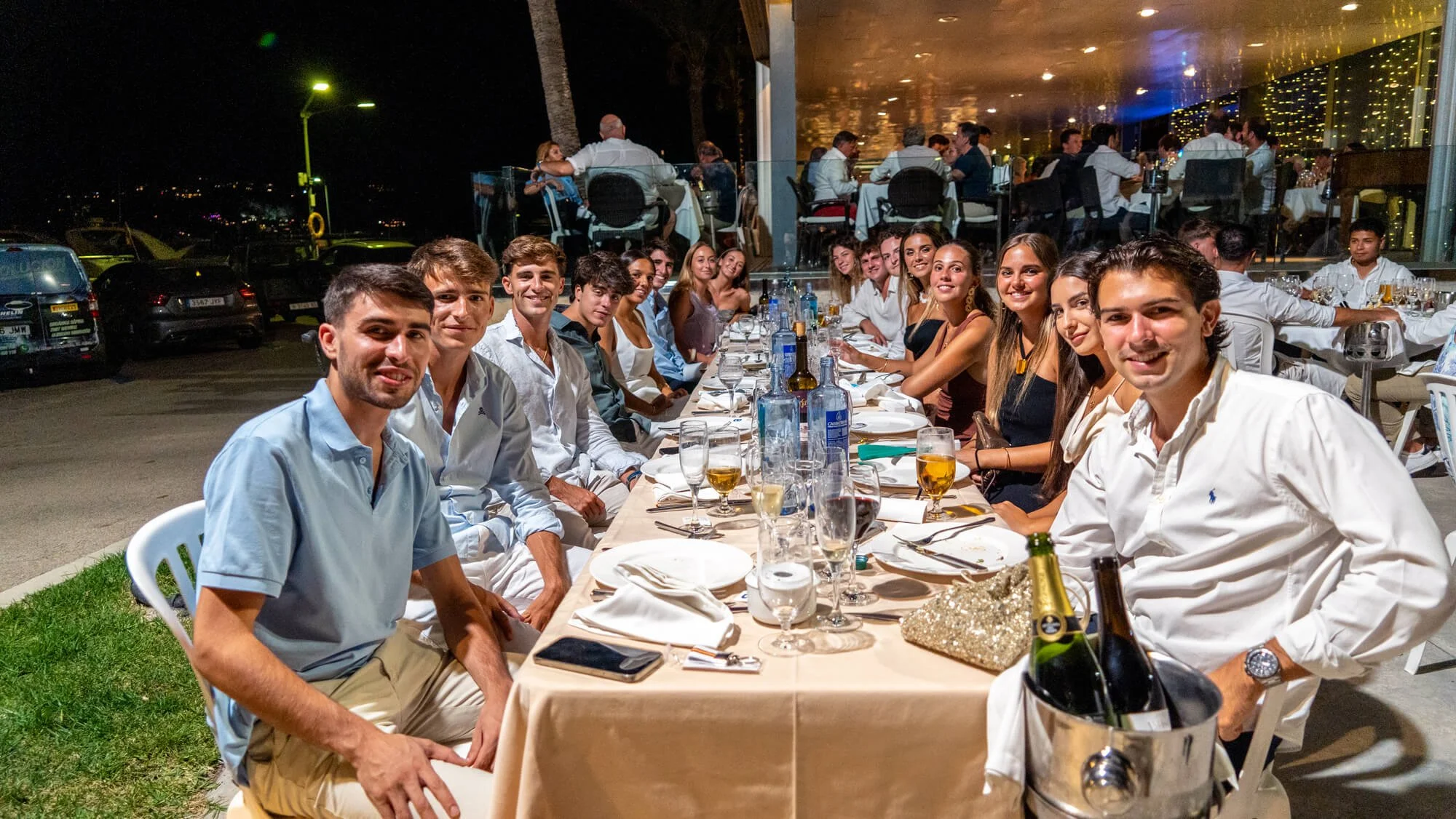 Grupo de personas sentadas en una mesa larga en un restaurante, posiblemente en una celebración, durante la noche, con un ambiente elegante y alegre.