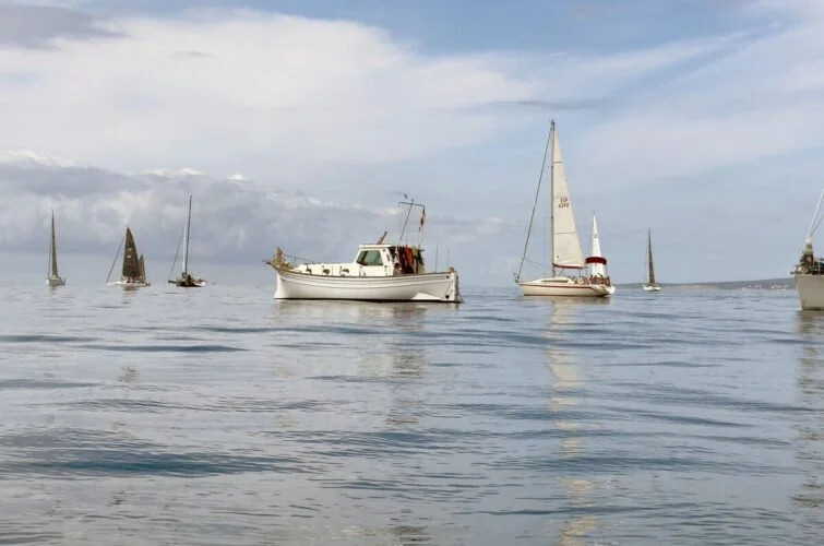 Varias embarcaciones en el mar, incluyendo un velero y un yate, con cielo parcialmente nublado.