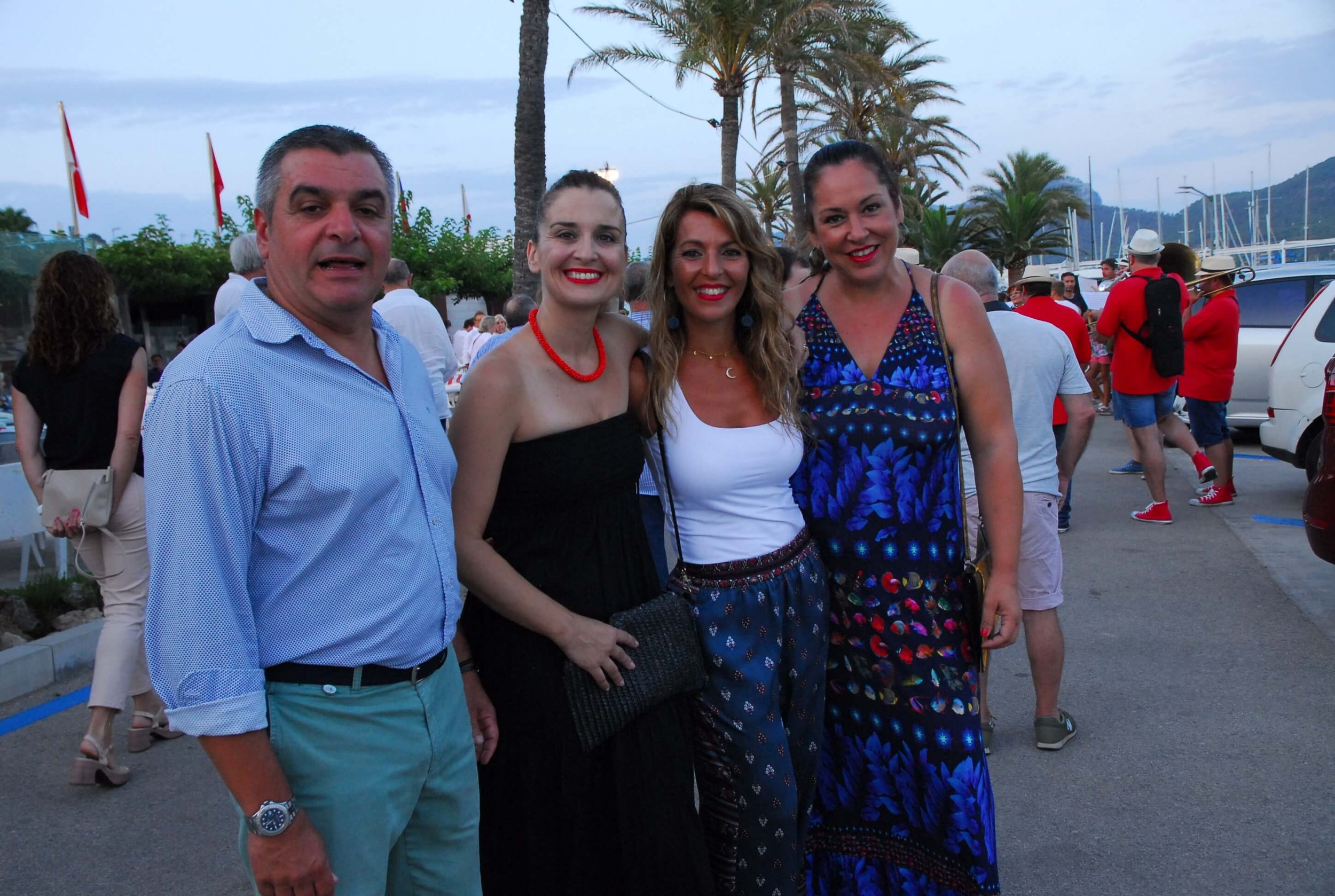Cuatro personas posando juntas en un evento al aire libre cerca del mar, con palmeras y barcos en el fondo, en la tarde.