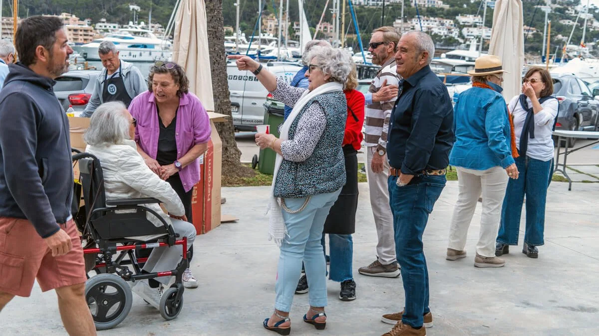 Grupo de personas conversando al aire libre cerca del puerto con yates y barcos en el fondo.