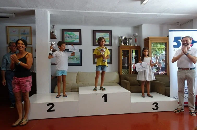 Niños en un podio recibiendo premios en una ceremonia de premiación, con adultos a los lados celebrando.
