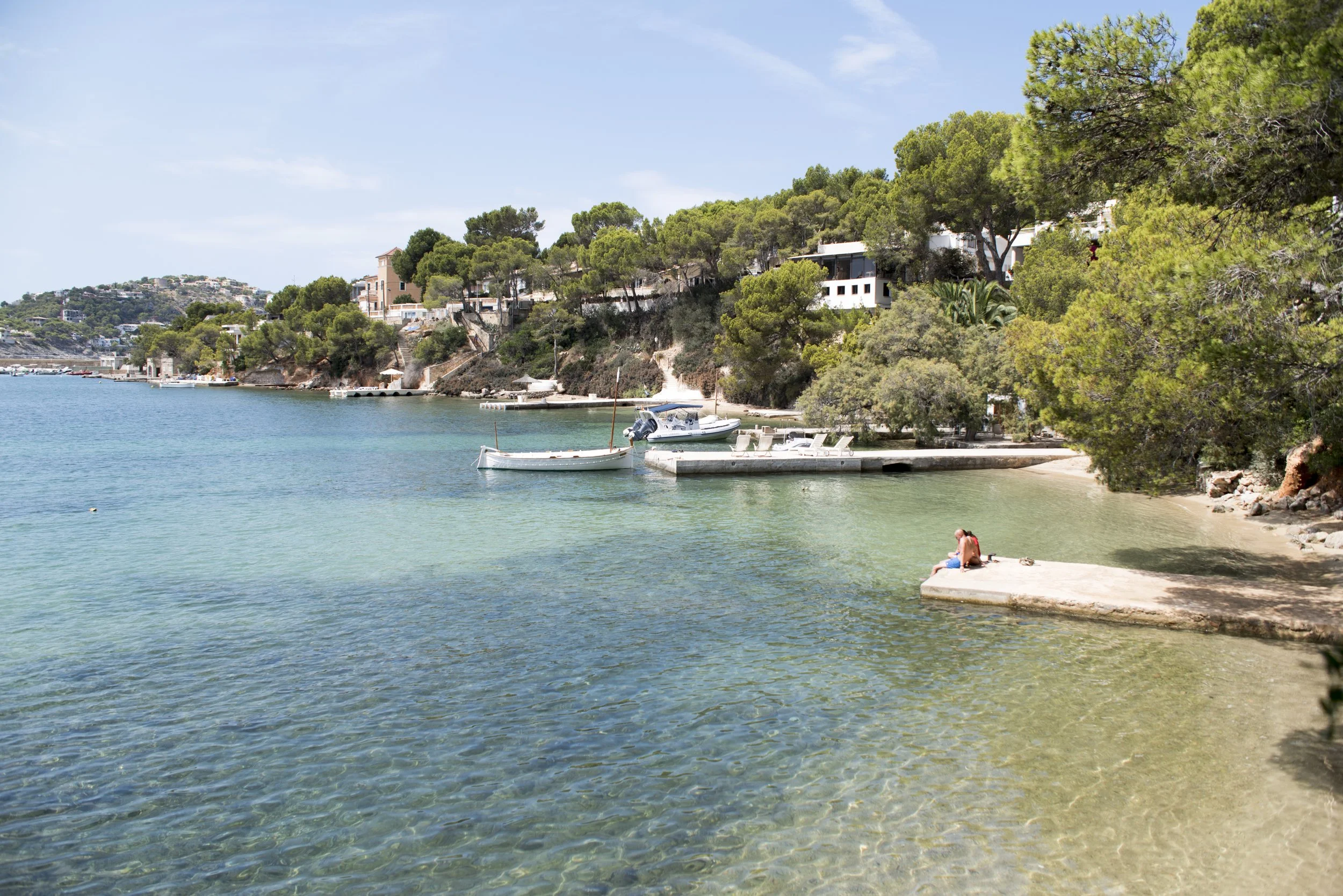 Vista de una playa con agua clara y verdes montañas con casas y árboles.