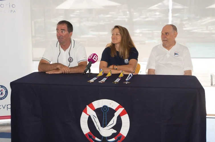 Tres personas sentadas en una mesa con medallas y un micrófono, en un evento de natación.
