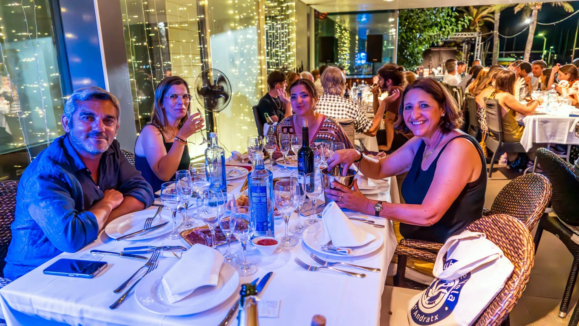Personas sentadas en una mesa decorada con luces en un restaurante, disfrutando una comida en una noche animada.