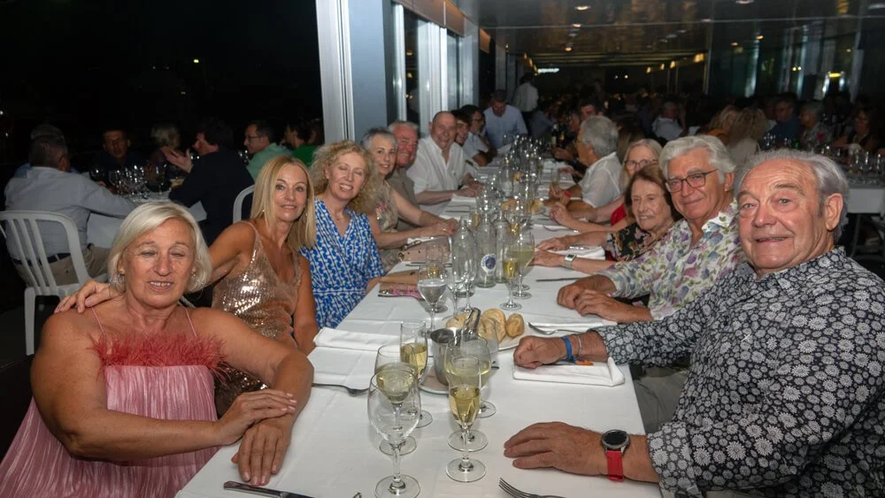 Grupo de personas sentadas en una mesa larga en un restaurante, celebrando un evento especial, con comida y bebidas en la mesa, en un ambiente elegante y concurrido.