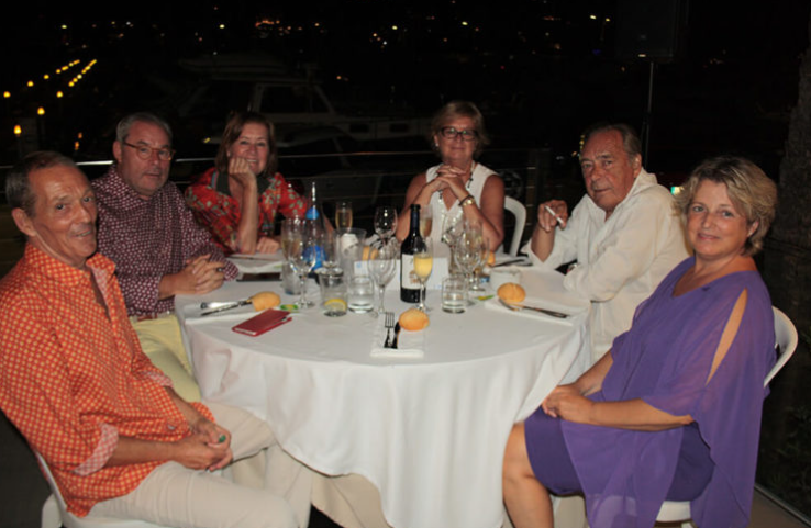 Seis personas adultas sentadas alrededor de una mesa en un restaurante, con comida y bebidas en la mesa, en un ambiente nocturno.