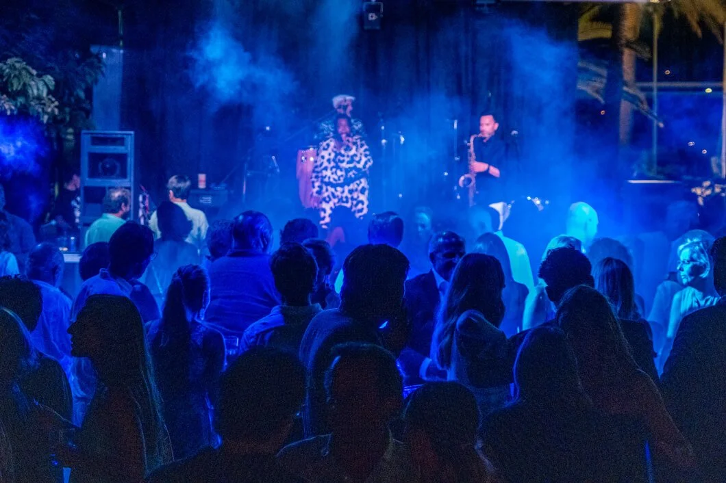 Gente en un evento en vivo con música en un ambiente oscuro, con luces azules y humo en el escenario.