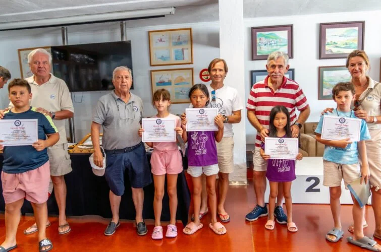 Niños y adultos en un evento de premiación, sosteniendo certificados, en un lugar con cuadros en las paredes.