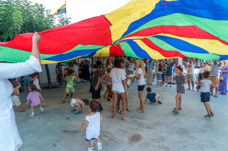 Niños y adultos jugando con un paracaídas multicolor en un espacio al aire libre, en una celebración o fiesta familiar.