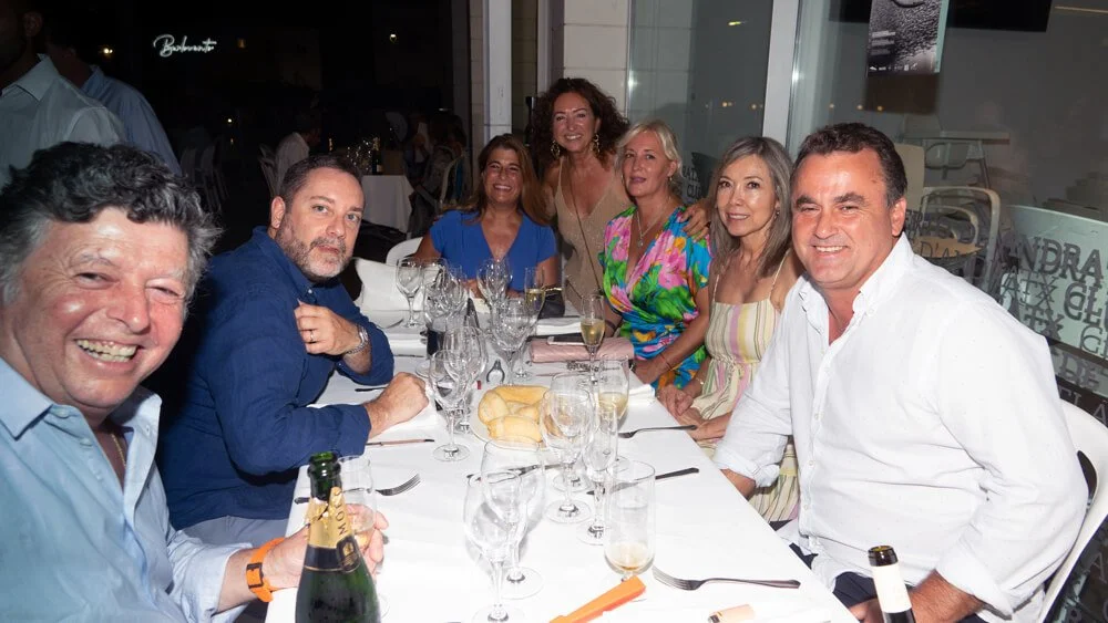 Grupo de personas sentadas en una mesa en un restaurante, sonriendo y disfrutando de la comida y la compañía.