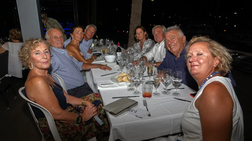 Grupo de personas adultas sentadas en una mesa de restaurante durante una comida o celebración nocturna.