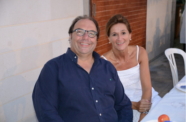 Una pareja sonriendo en una mesa, en un entorno exterior, con decoración moderna y un fondo de pared de ladrillos y otra de concreto.