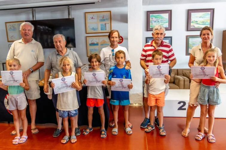 Grupo de niños y adultos en una ceremonia, algunos sosteniendo certificados, en un espacio con pinturas en las paredes.