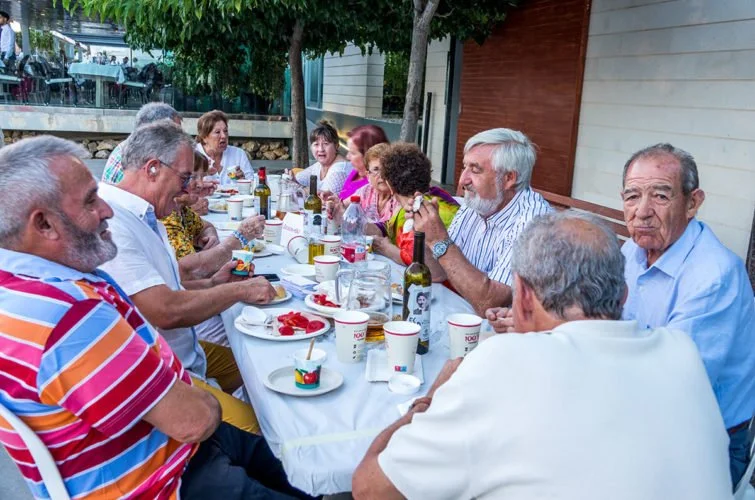 Grupo de personas mayores sentadas alrededor de una mesa en una comida al aire libre.