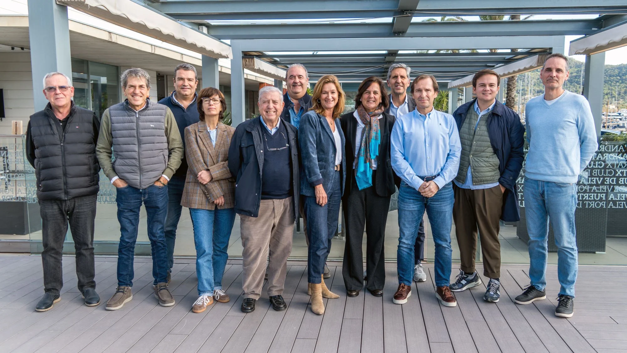 Grupo de personas adultas posando para una foto al aire libre frente a un edificio con techo de metal y vistas de palmeras.