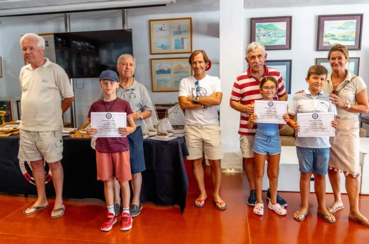 Grupo de personas, adultos y niños, posando con certificados en un evento interior, decorado con pinturas en las paredes.