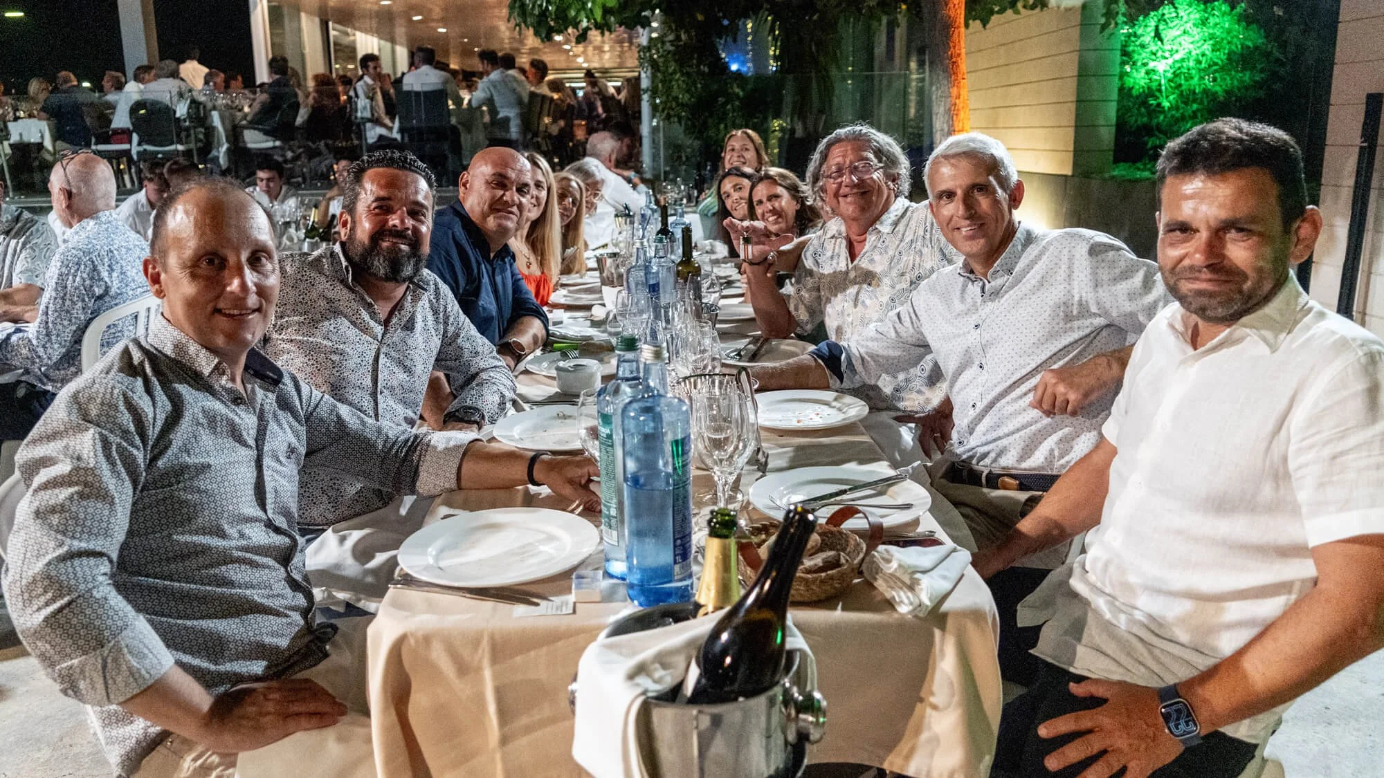 Grupo de personas sentadas en una mesa de restaurante, brindando y sonriendo, en un ambiente elegante y festivo por la noche.