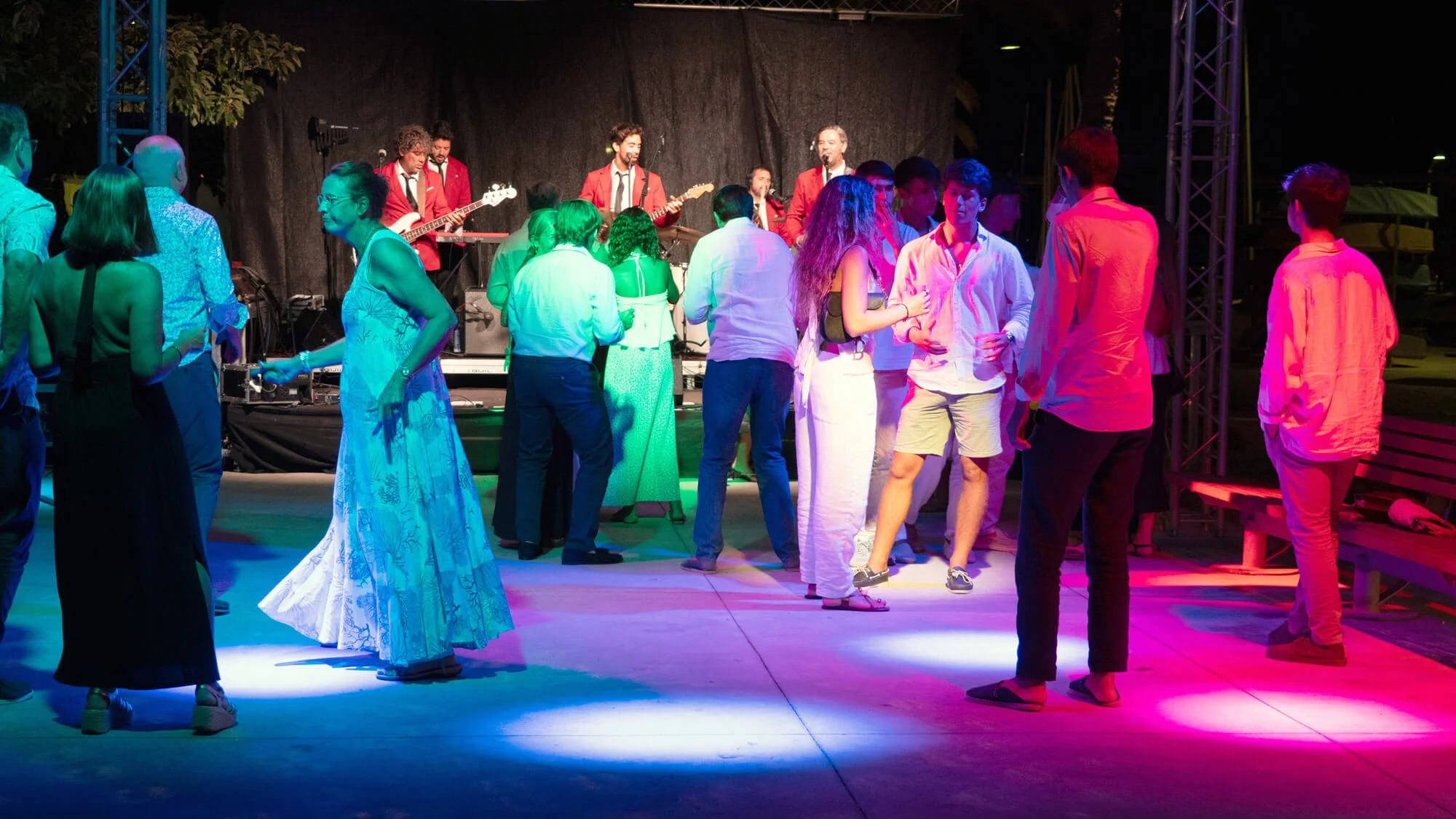 Personas bailando y disfrutando en un concierto con banda en vivo en un escenario iluminado con luces de colores.