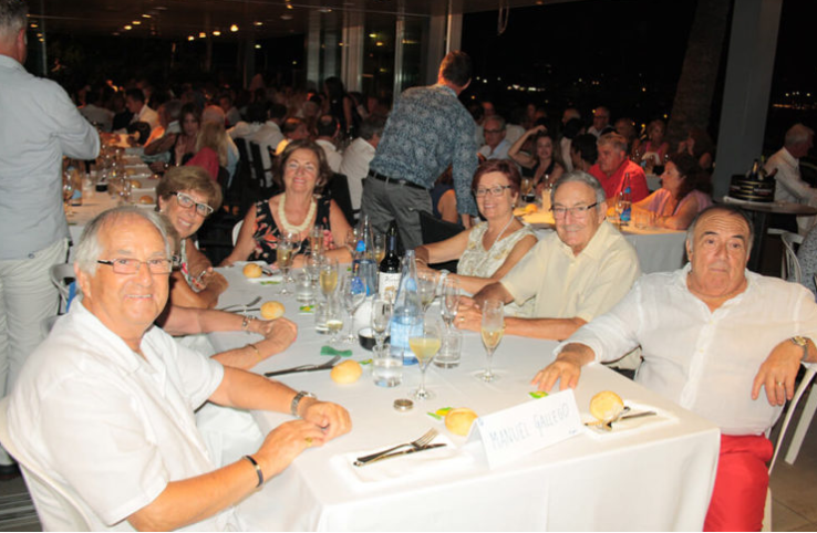 Grupo de personas sentadas en una mesa en una celebración o cena formal en un restaurante elegante, con comida y bebidas sobre la mesa.