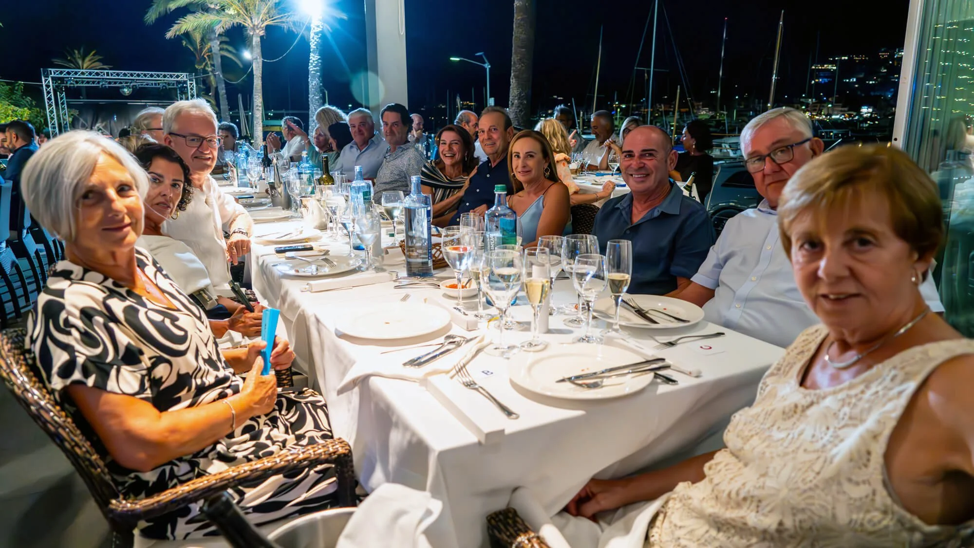 Grupo de personas sentadas en una mesa en una cena al aire libre durante la noche en un puerto.