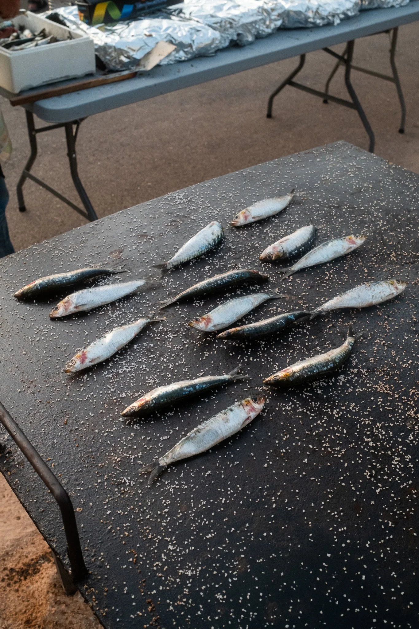 Pescados pequeños sobre una mesa negra con semillas de sésamo, en un mercado al aire libre.