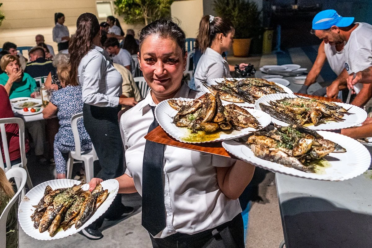 Una mujer lleva varias bandejas con pescado asado durante una comida en grupo al aire libre.