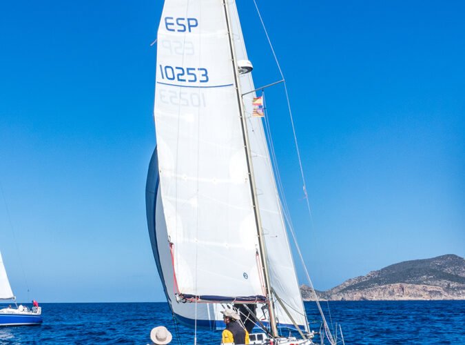 Velero navegando en el mar con un cielo despejado y tierra al fondo.