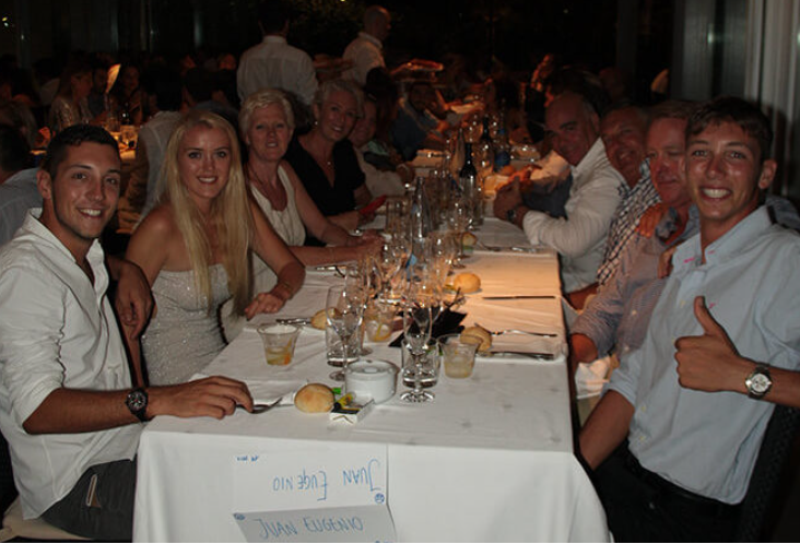 Grupo de personas sentadas en una mesa en un restaurante o evento, con bebidas y comida en la mesa, en un ambiente elegante y bien iluminado.