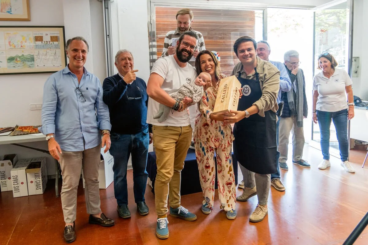 Grupo de personas en una sala, celebrando la llegada de un bebé, con algunos entregando un obsequio a los padres del niño.