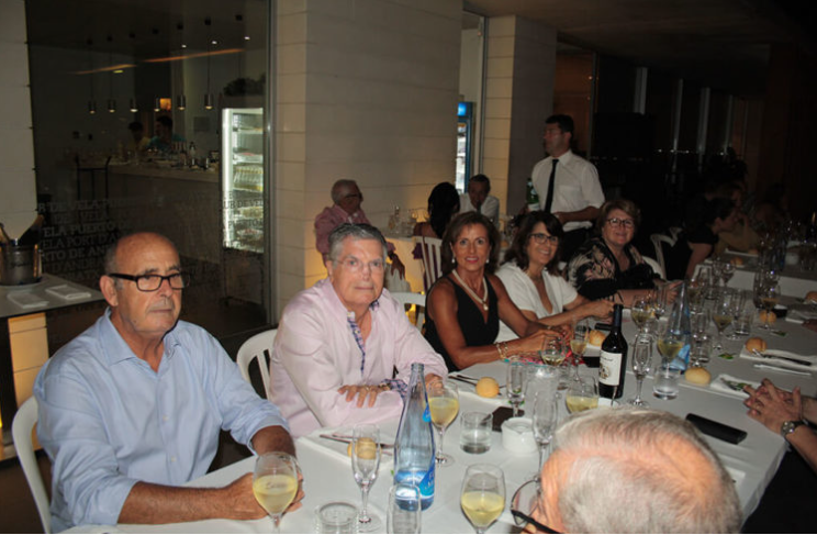 Personas sentadas en una mesa en un restaurante, disfrutando de una comida y bebidas, en un ambiente elegante y social.